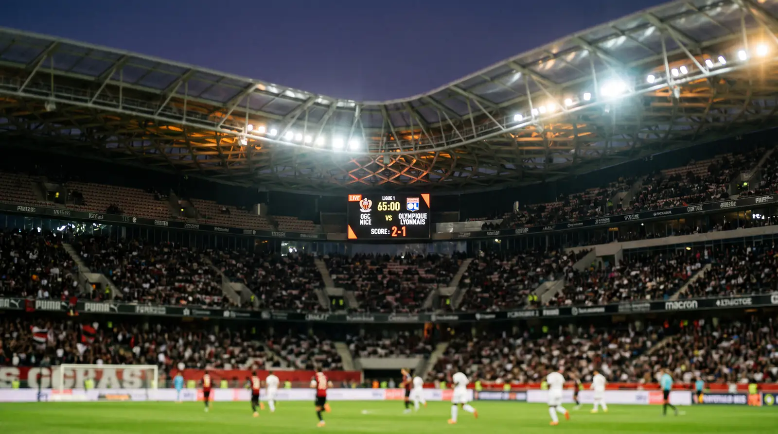 Stade de football français illuminé le soir avec tableau d'affichage numérique montrant les cotes en temps réel